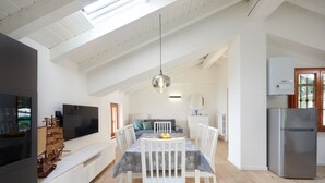 Un comedor espacioso con techo alto, una lámpara moderna y un televisor plano grande a la izquierda.