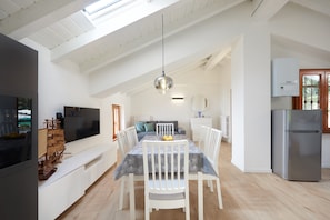 Un vaste espace dédié à la salle à manger, doté d’un haut plafond, d’un lustre moderne et d’un grand téléviseur à écran plat placé sur le côté gauche.
