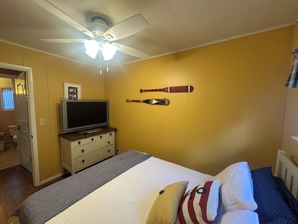 A bedroom with a bed, a television on a dresser, a ceiling fan, and two baseball bats on the wall. - Tranquil waterfront retreat 3-bedroom house with WiFi in charming Bath NY (Bath)