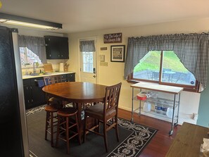 A kitchen with a wooden table and chairs, a window with checkered curtains, and a door with a welcome sign. - Tranquil waterfront retreat 3-bedroom house with WiFi in charming Bath NY (Bath)