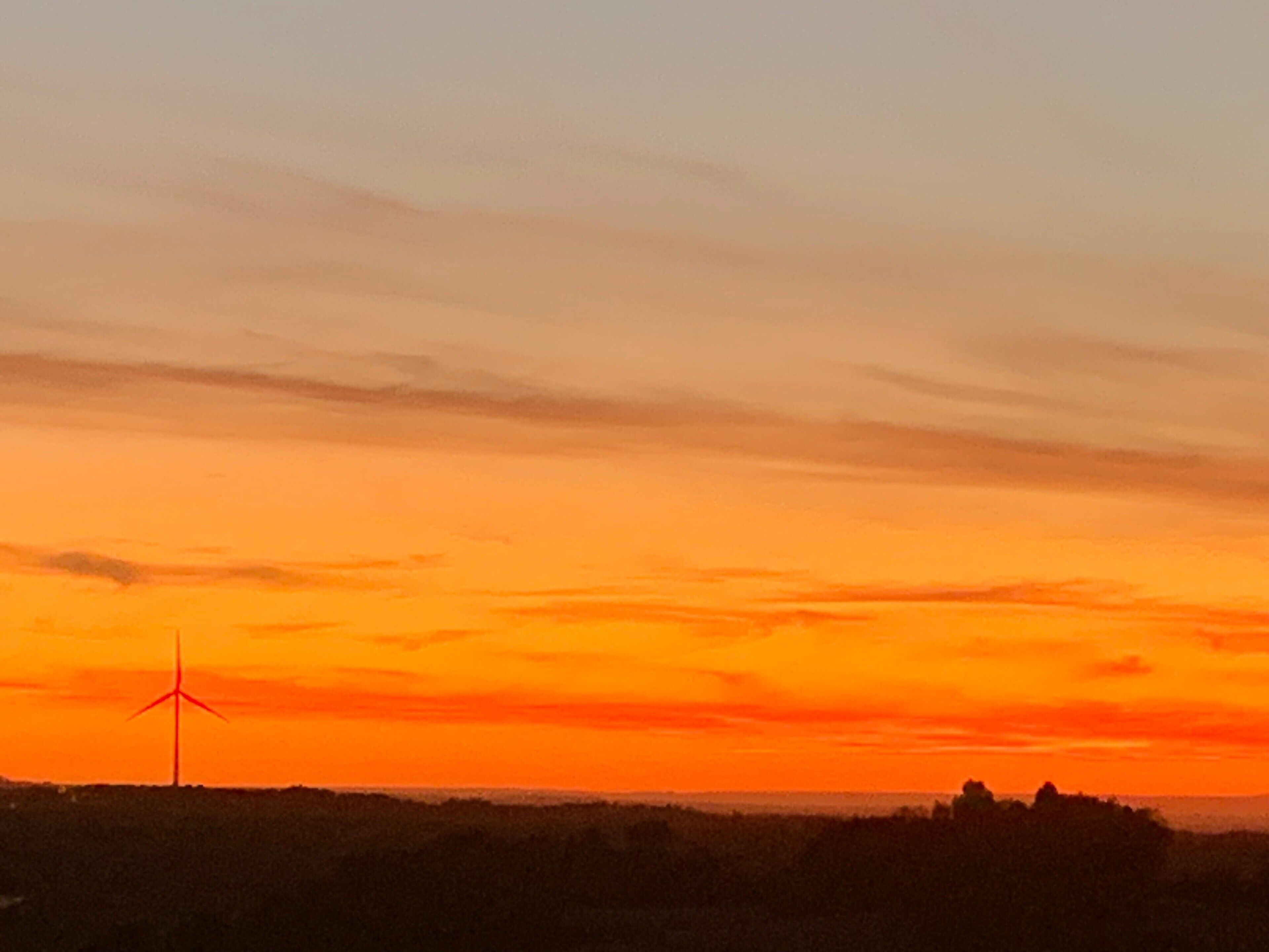 A sunset with a wind turbine in the foreground.