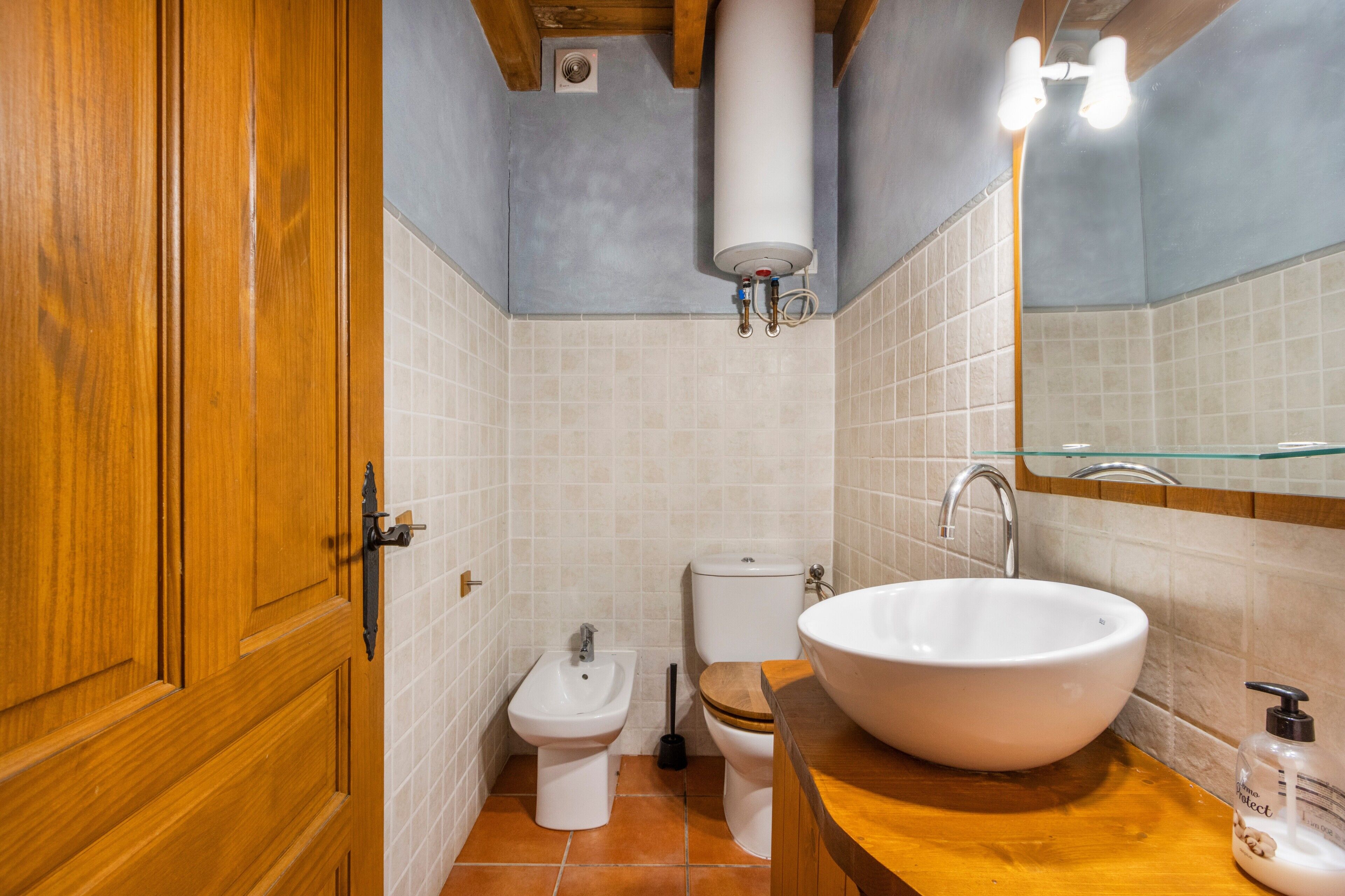 A bathroom with a wooden door, a white sink, a bidet, and a toilet.
