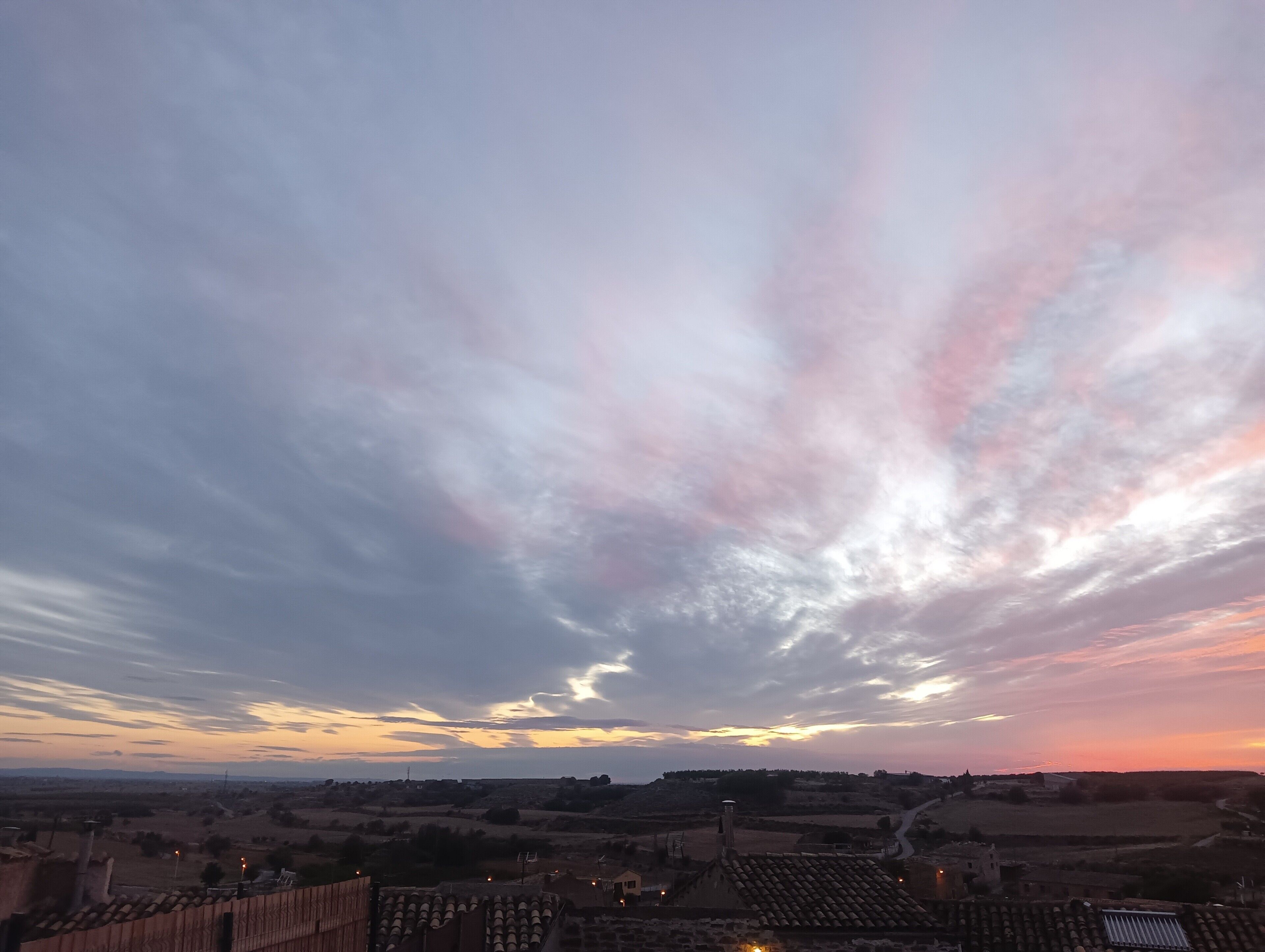 Paesaggio rurale con cielo al tramonto, tetti in terracotta e edifici sparsi.
