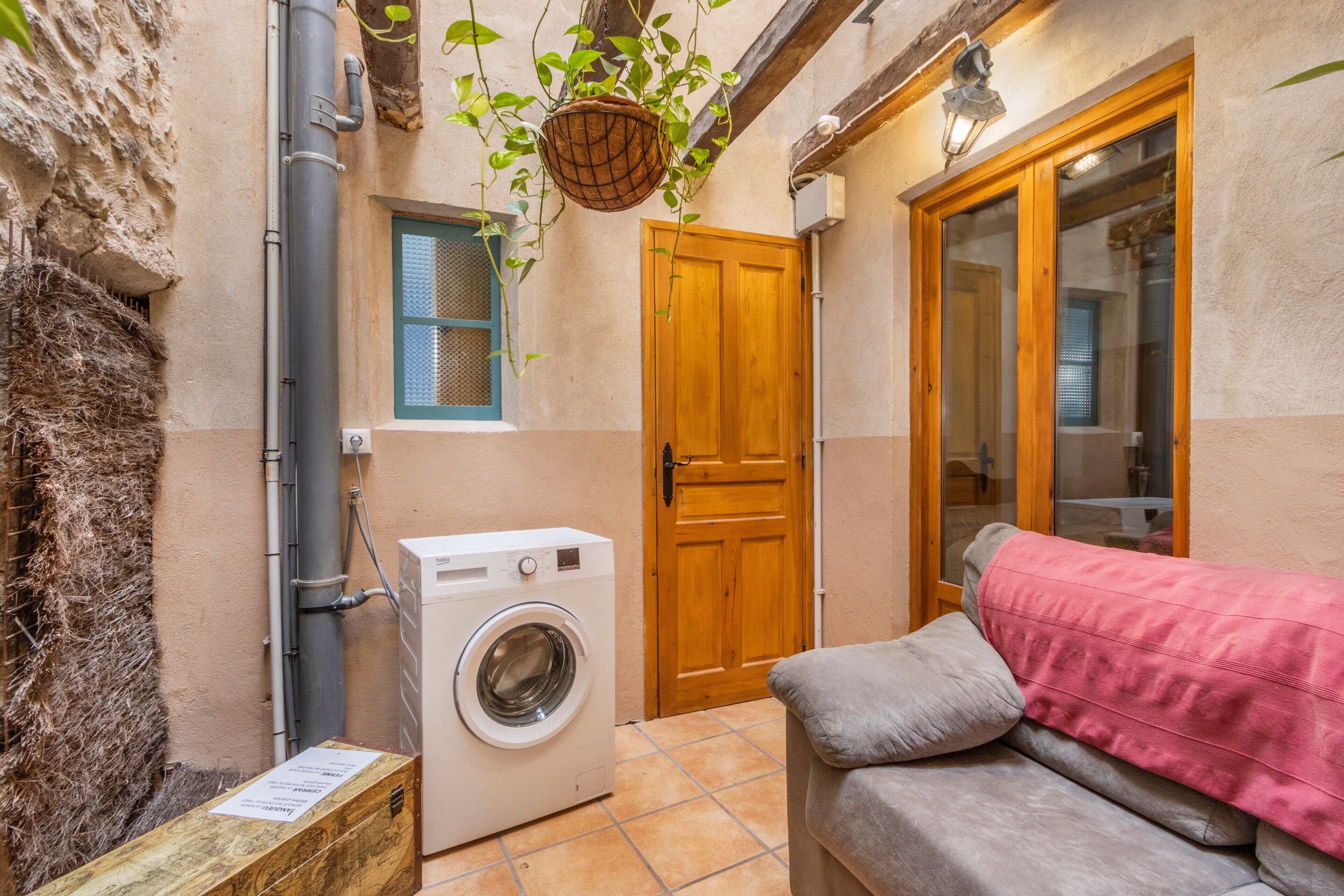 A laundry area with a washing machine, a wooden door, and a couch with a pink blanket.
