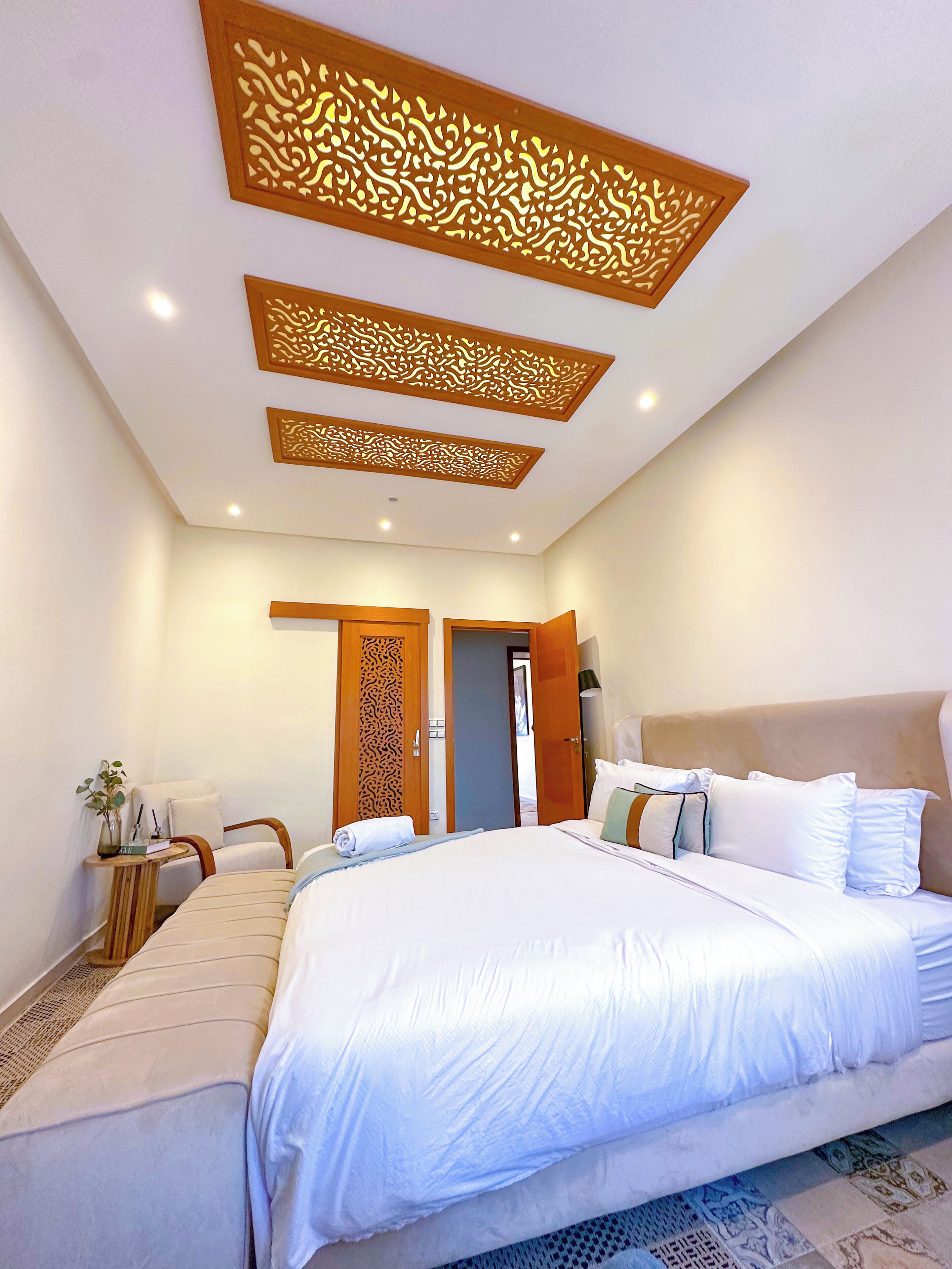 Une chambre d’hôtel moderne avec un grand lit, une table de chevet, une lampe et un panneau décoratif au plafond.