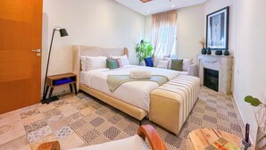 A modern bedroom with a large bed, a bedside table, a floor lamp, a potted plant, and a fireplace. - Downtown Gem - View of the old medina (Rabat)
