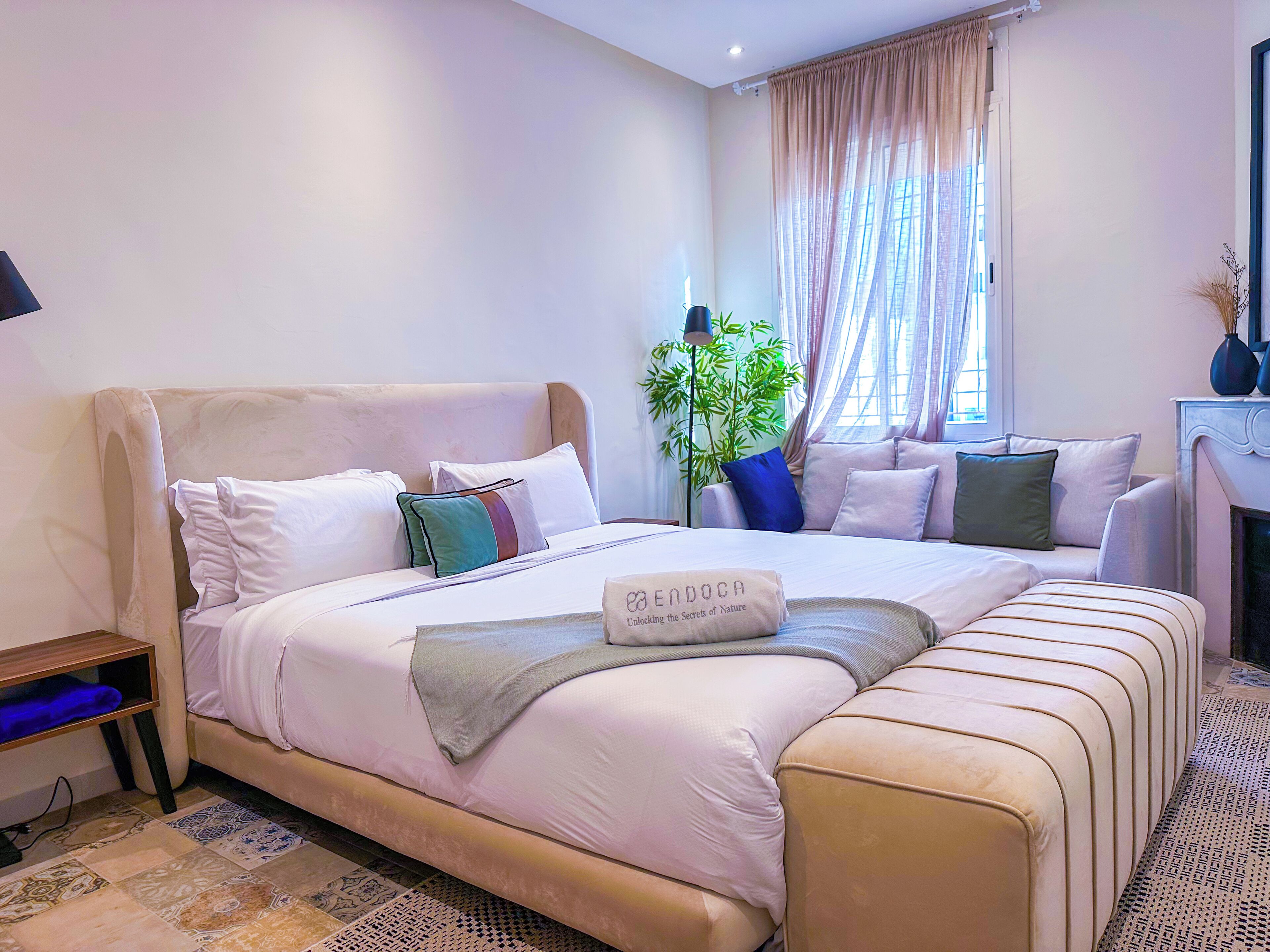 A neatly arranged bedroom with a large bed, a bedside table, a lamp, and a window with curtains.