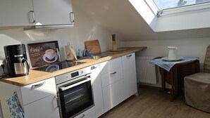 A compact kitchen with white cabinets, a wooden countertop, a coffee maker, a kettle, and a small table with a pitcher. - Cozy vacation apartment near Bamberg, dogs welcome! (Bischberg)