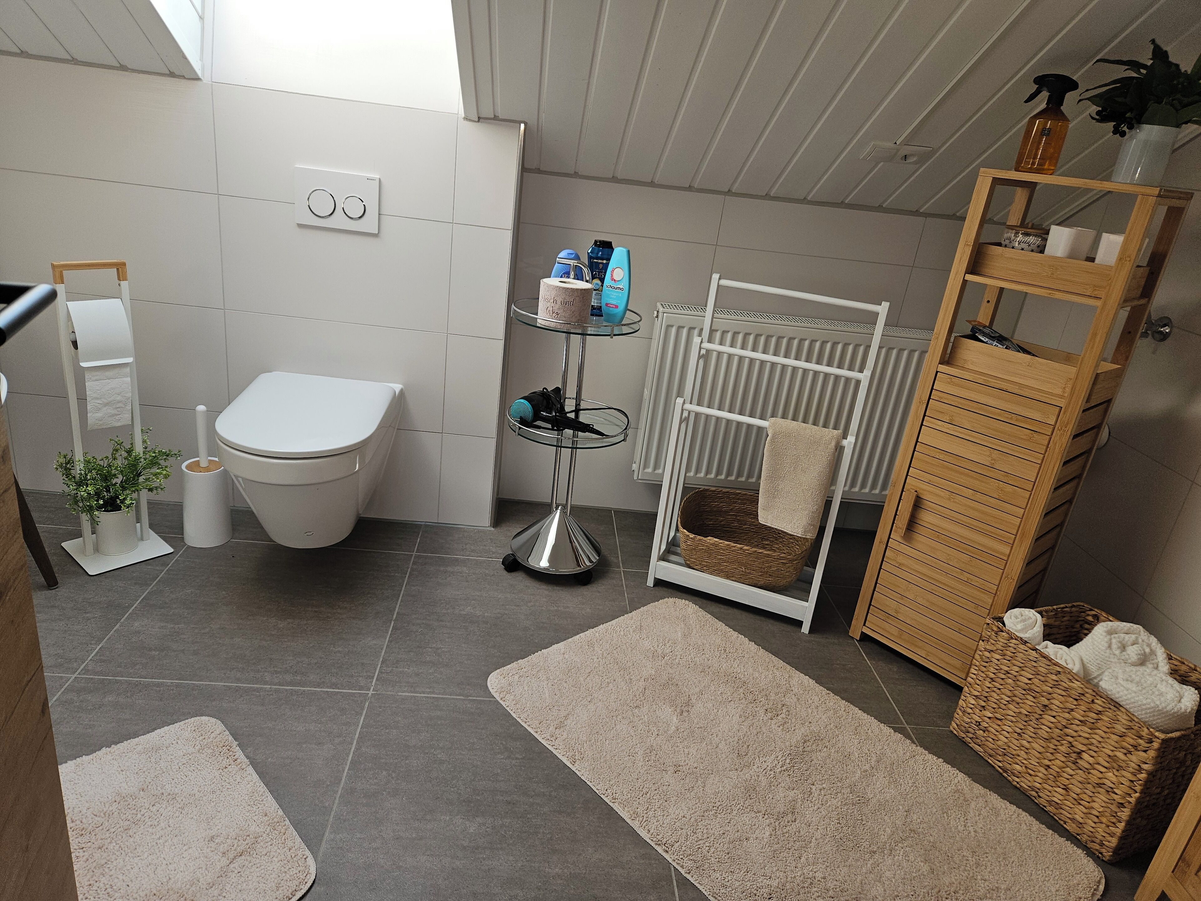 A modern bathroom with a toilet, bidet, towel rack, and a small table with toiletries.