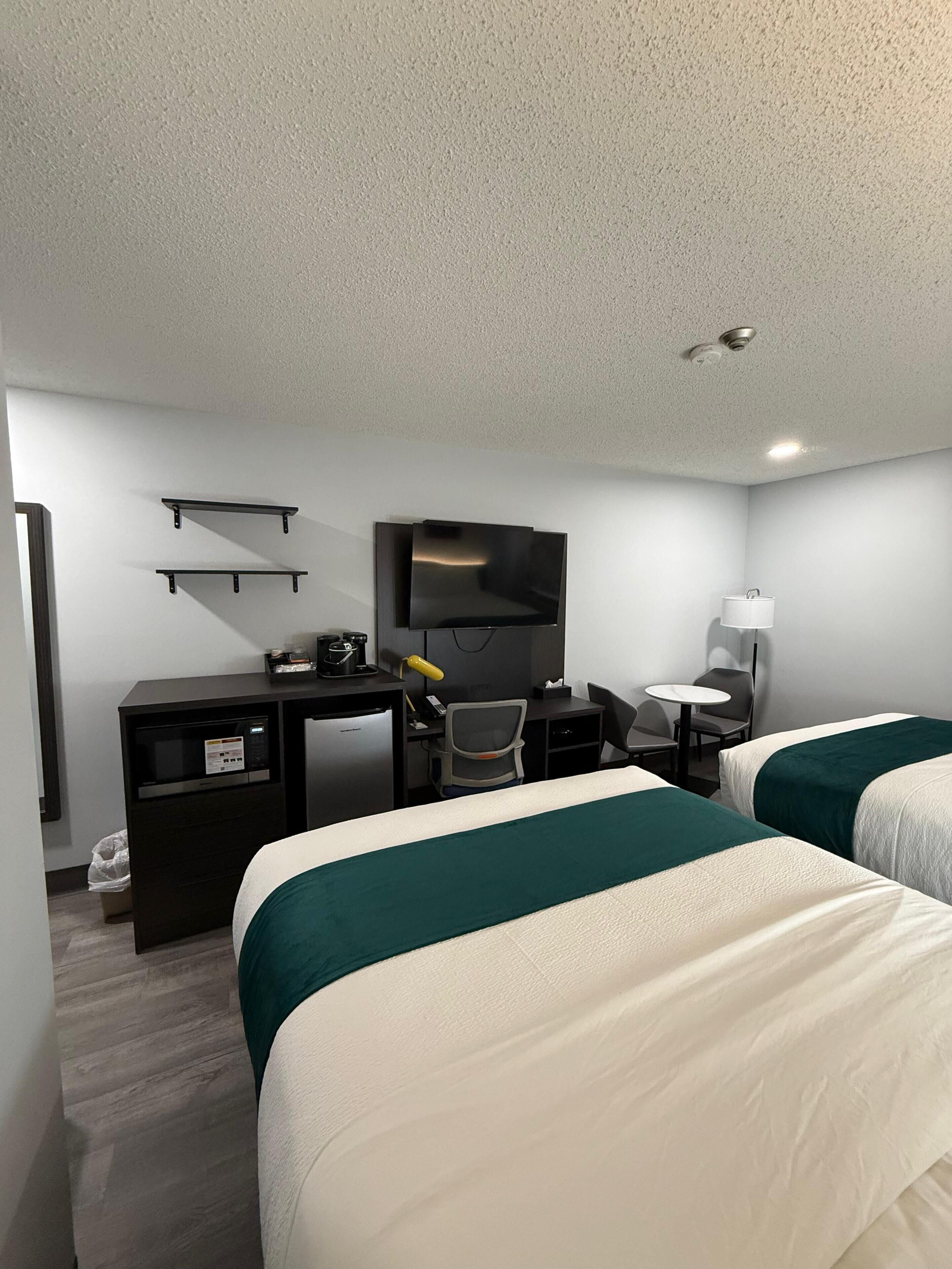 A hotel room with two beds, a desk with a computer, a TV, and a small table with a lamp.