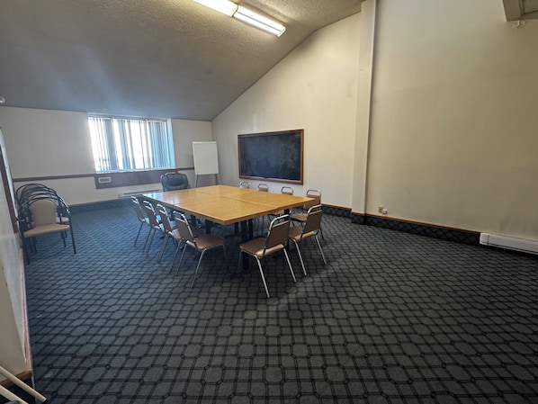 Une salle de conférence équipée d’une grande table, de chaises, d’un tableau blanc et d’une fenêtre avec des stores.
