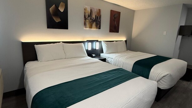 A hotel room with two beds, a nightstand, a lamp, and artwork on the wall. - Zero-100 Motor Inn (Marathon)