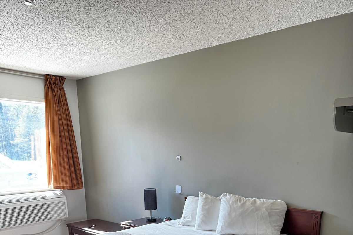 A bedroom with a large bed, a bedside table, a lamp, and a window with curtains.