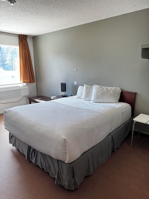 Une chambre à coucher avec un grand lit, une table de chevet, une lampe et une fenêtre avec des rideaux.