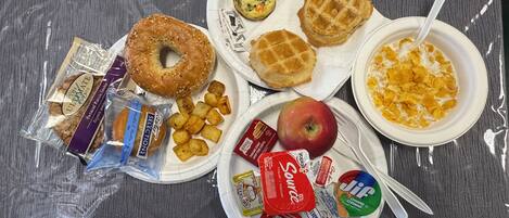 A meal with a bagel, waffles, a bowl of cereal, a donut, and various snacks.