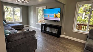 A living room with a flat-screen TV on a stand, a grey sofa, and a wooden floor.