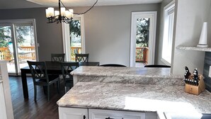 A kitchen with a granite countertop, wooden chairs, and a chandelier.