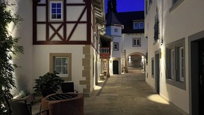 Une ruelle étroite bordée de maisons traditionnelles à colombages, avec un banc en pierre et un pot de fleurs.