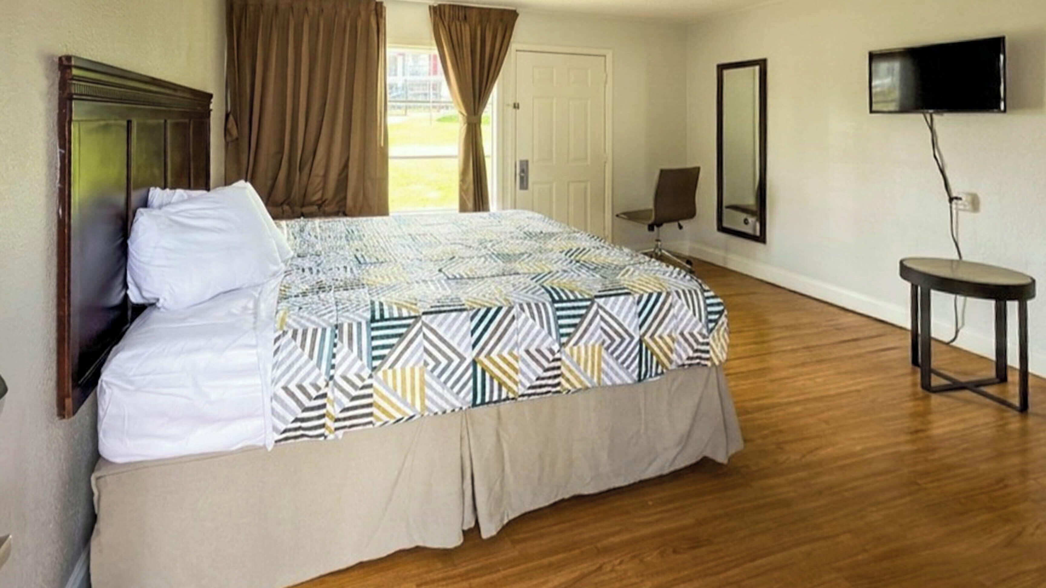 A hotel room with a bed, a TV, a chair, and a small table.