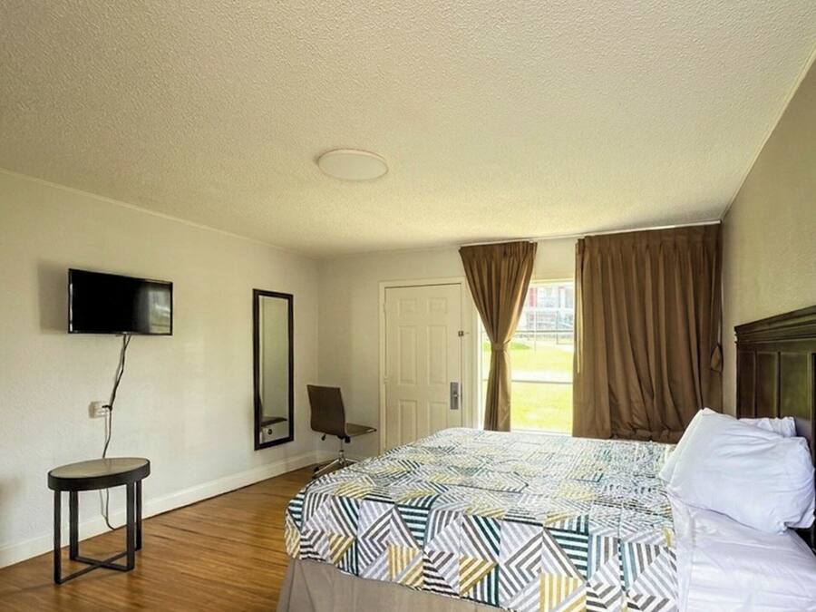 Camera d'albergo con un letto, una televisione a parete, un tavolino rotondo, una sedia e una porta.