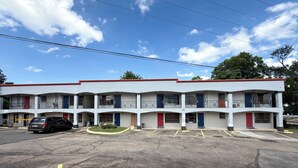 Un motel de varios pisos con estacionamiento, con una decoración en rojo y blanco, y un cielo azul despejado.