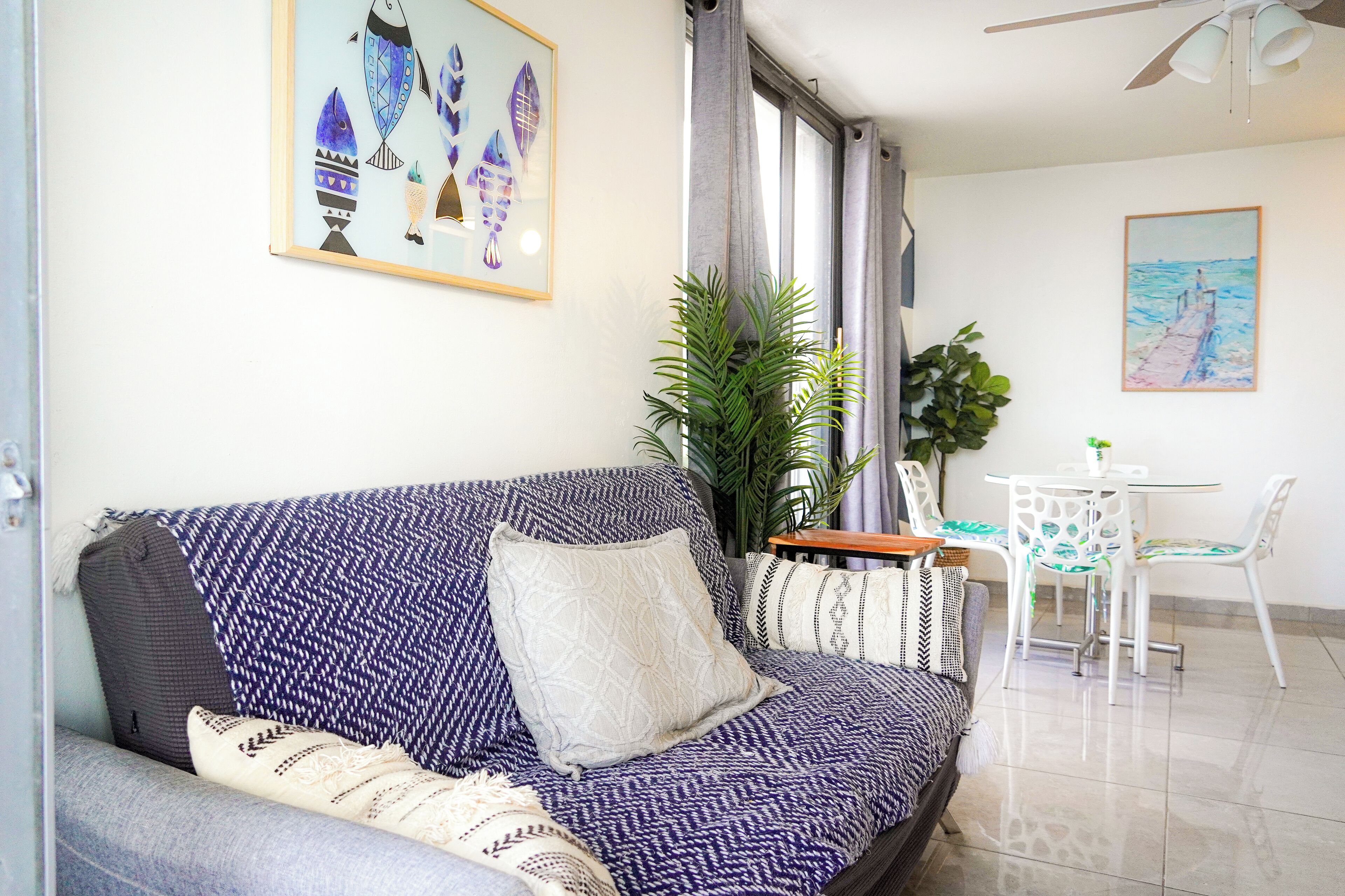 A modern living room with a sofa, a dining table with chairs, and a large window with curtains.
