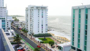 A coastal hotel with multiple floors, a beach view, and a street with cars and palm trees. - Modern 1-Bedroom in the Heart of Condado with Stunning Ocean Views (San Juan)