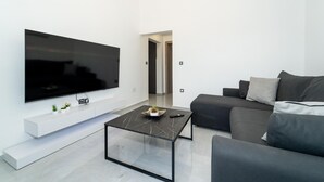 A modern living room with a flat-screen TV mounted on the wall, a glass coffee table, and a grey sofa with cushions. - 1 bedroom gorgeous apartment in Pridraga (Pridraga)