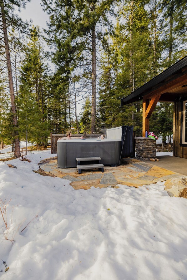 A hot tub in a snowy outdoor setting with a stone patio and wooden deck.