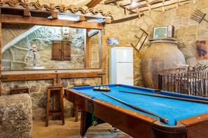 A pool table with a blue felt surface, a wooden chair, a stone wall, and a vintage television. - Country House 'El Rincón Del Duende' with Mountain View, Wi-Fi and Air Conditioning (Pedro Bernardo)