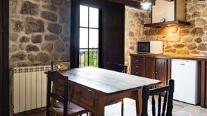 A rustic kitchen with a stone wall, wooden table, and a white refrigerator.