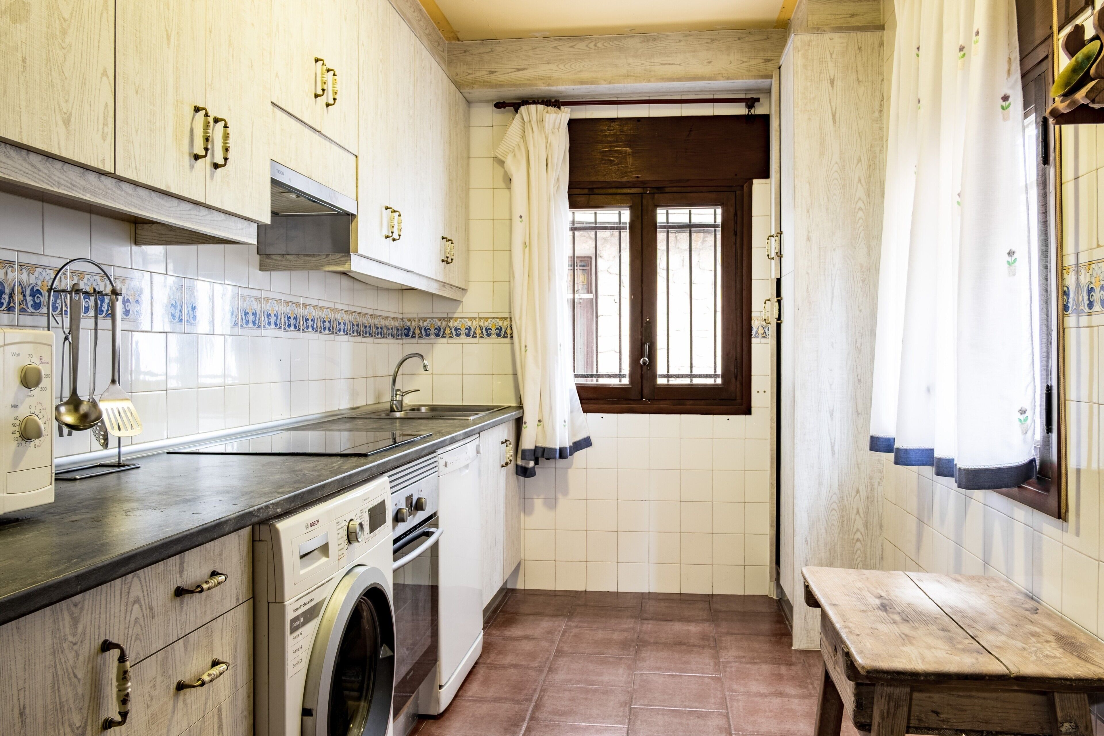 A compact kitchen with a washing machine, a sink, and a wooden bench.