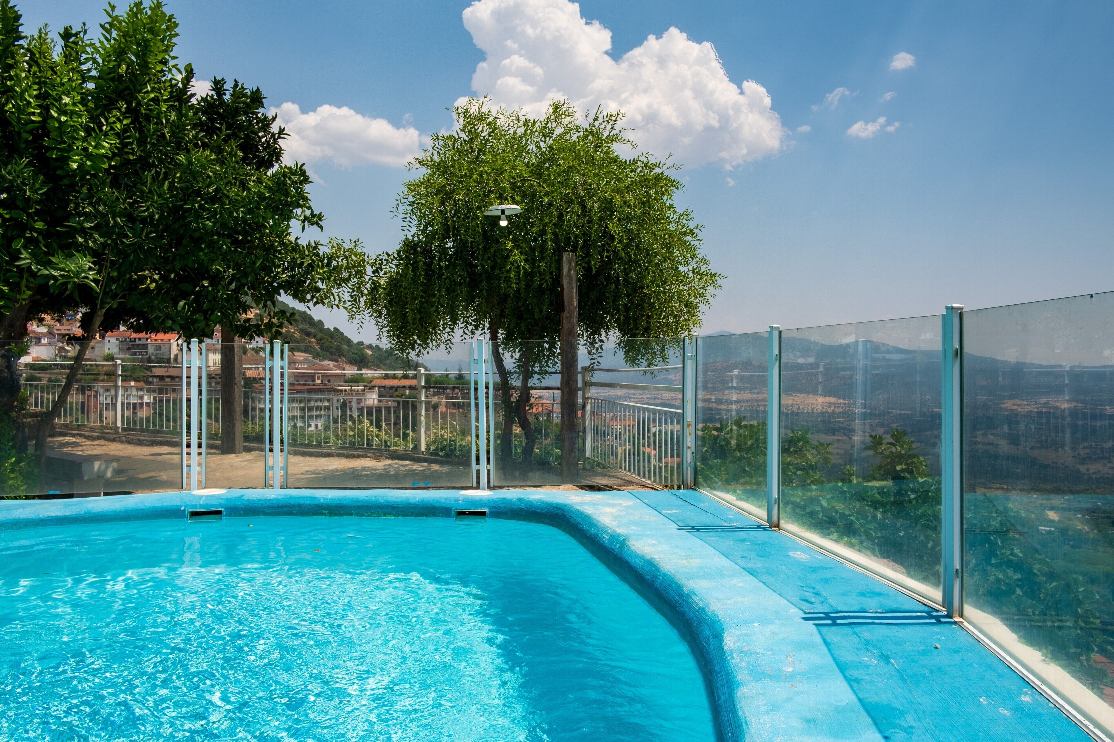 Ein Pool mit Glasbarriere, Bäumen und Blick auf Gebäude im Hintergrund.