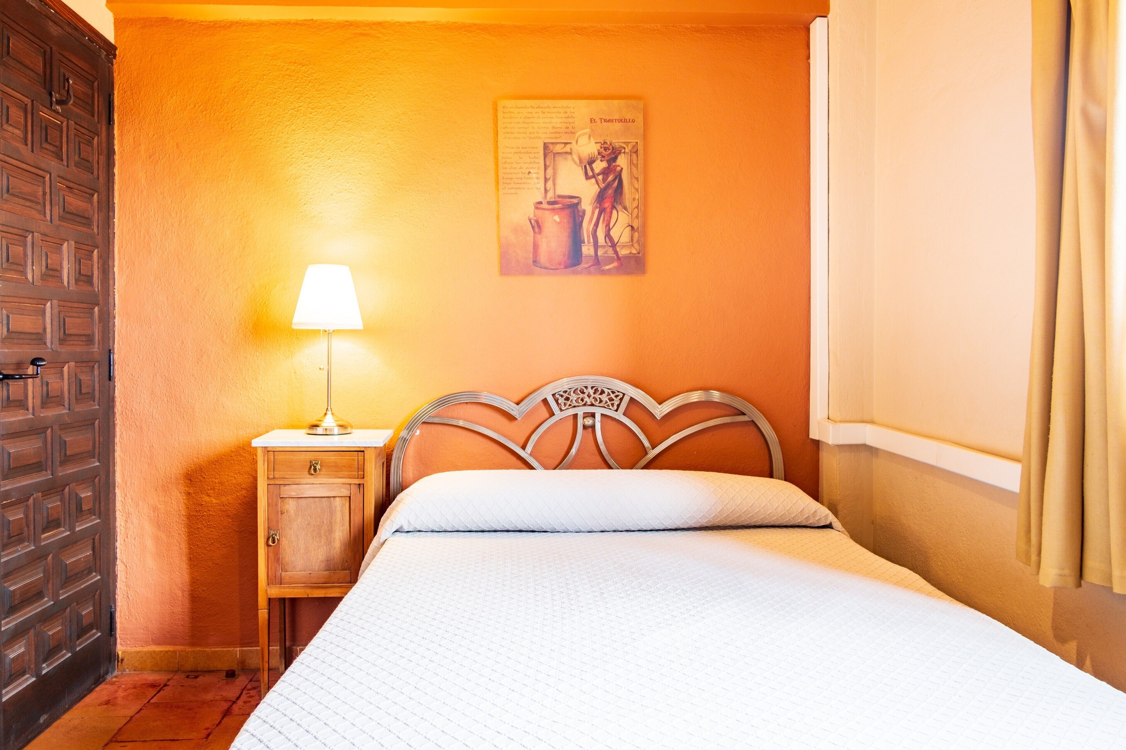 Une chambre d’hôtel avec un lit, une table de chevet avec une lampe, une armoire en bois et une affiche accrochée au mur.