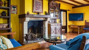 A room with a fireplace, wooden furniture, a glass table, and a television mounted on the wall.