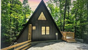 Una baita con tetto triangolare, un patio in legno e un'ampia finestra.