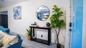 A modern living room with a black console table, a round mirror, a blue sofa, and a large potted plant. - Charming 3BR Miami Home with Stylish Lounge, Coffee Bar & Peaceful Vibes (Miami)