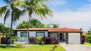 A two-story house with a red-tiled roof, a garage, and a well-maintained lawn with palm trees and shrubs. - Charming 3BR Miami Home with Stylish Lounge, Coffee Bar & Peaceful Vibes (Miami)