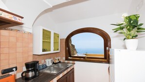 Una cucina con vista sul mare attraverso una finestra, dotata di macchina per il caffè, tostapane e una pianta in vaso.