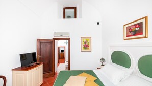Una camera da letto con un letto, una televisione su un mobile, una piccola finestra e una porta che conduce a un'altra stanza.