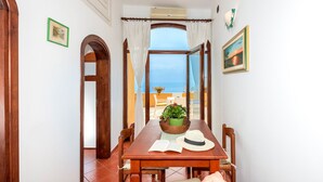 Zona pranzo con tavolo in legno, sedie e vista sul mare attraverso un'ampia finestra.