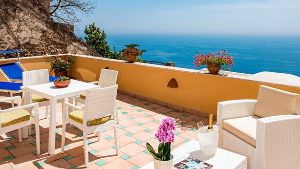 Una terrazza con mobili in vimini bianco, vista sul mare e una scogliera rocciosa.