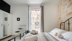 Una camera da letto con un letto, un armadio, un tavolino con una sedia e vista attraverso una finestra con una porta decorativa.