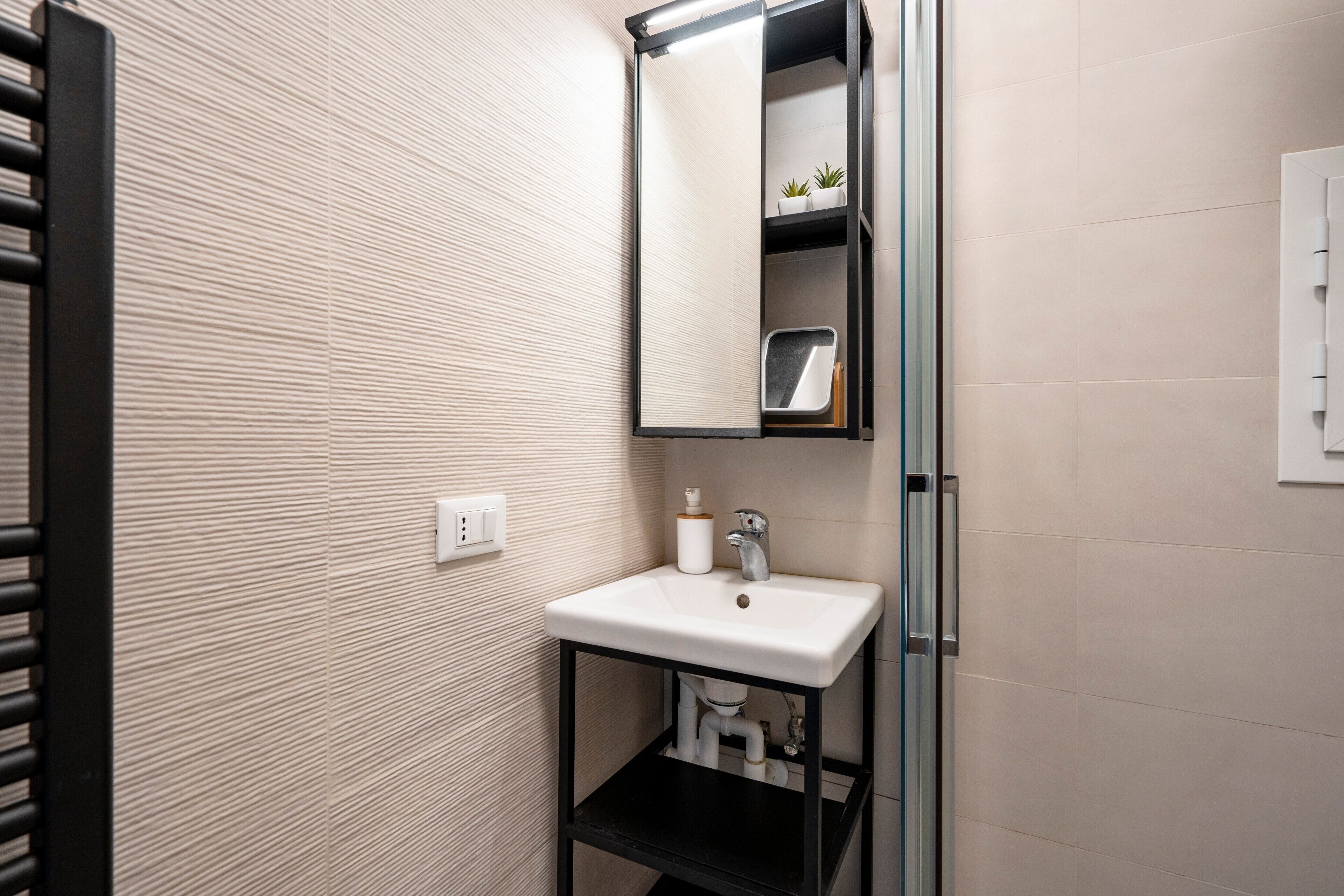 A bathroom with a white sink, a mirror, and a shelf with plants.