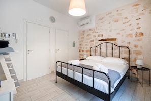 A bedroom with a bed, a bedside table, a lamp, a wall clock, and a door.