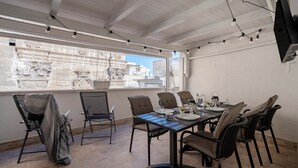 A dining area with a table set for four, surrounded by chairs, a TV mounted on the wall, and string lights.