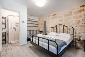 A bedroom with a bed, a shower, a bedside table, and a wall with a stone pattern.