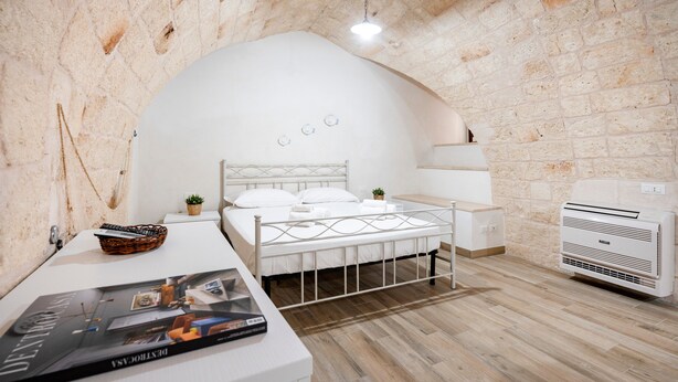A bedroom with a white bed, a bedside table, a wall-mounted heater, and a brick wall. - Apartment 'Casa Sardella, Nel Centro Storico' with Wi-Fi and Air Conditioning (Monopoli)