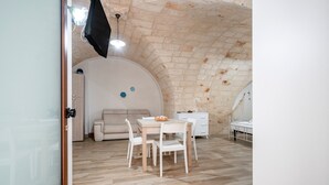 A room with a wooden floor, a white table with chairs, a sofa, a bed, and a TV mounted on the wall. - Apartment 'Casa Sardella, Nel Centro Storico' with Wi-Fi and Air Conditioning (Monopoli)