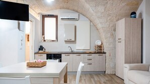 A modern kitchen with a stone arch, white cabinetry, and a dining area with a table and chairs. - Apartment 'Casa Sardella, Nel Centro Storico' with Wi-Fi and Air Conditioning (Monopoli)